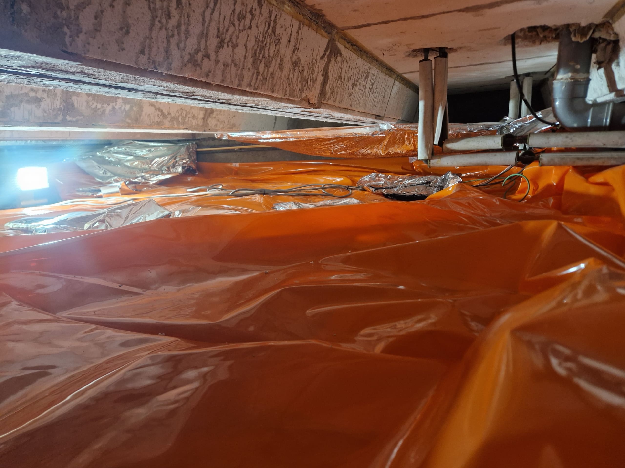 Eindresultaat vloerisolatie kruipruimte Tilburg met thermokussens Kruipruimte met oranje thermokussens netjes aangebracht tegen de onderzijde van de vloer in Tilburg